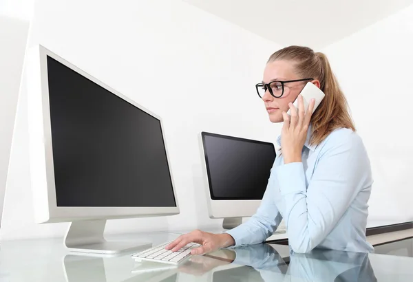 Женщина в офисе за столом перед экраном компьютера, разговаривает на — стоковое фото