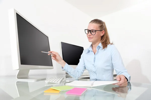 Женщина в офисе за столом с карандашом, указывающим на монитор — стоковое фото