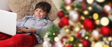 Mutlu Noeller, çocuk evde bilgisayarla aydınlanmış ve dekore edilmiş ağacın yanında.
