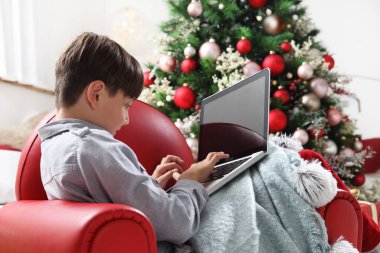 Mutlu Noeller, çocuk evde bilgisayarla aydınlanmış ve dekore edilmiş ağacın yanında.