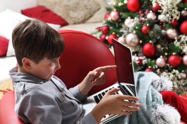 Mutlu Noeller, çocuk evde bilgisayarla aydınlanmış ve dekore edilmiş ağacın yanında.