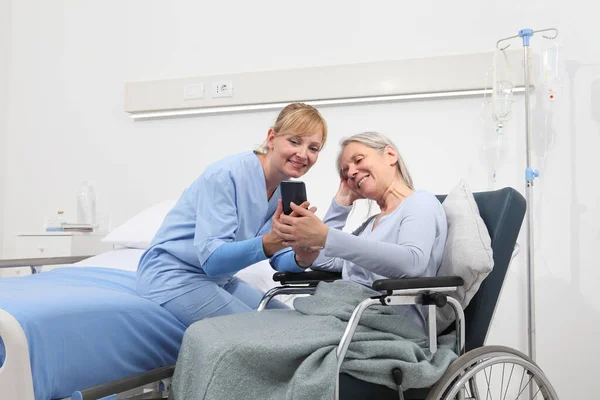 Nurse Helps Cell Phone Contact Elderly Lady Family Wheelchair Bed — Stock Photo, Image