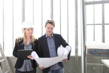 Erkek ve kadın mimarlar ya da mühendisler birlikte çalışarak inşaat alanının planlarını tartışırlar.