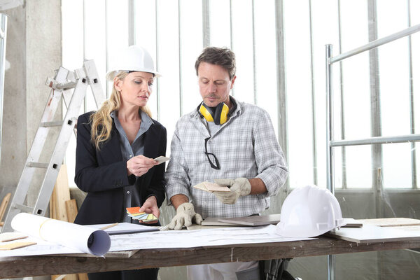 man and woman architect interior designer and foreman worker together with color samples and decorative materials discussing the project for interior decoration in the inside the construction building site
