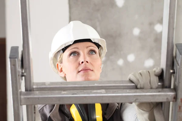 建筑工人中的女建筑工人 戴着白色头盔 在室内建筑背景上戴着听觉保护耳机 — 图库照片