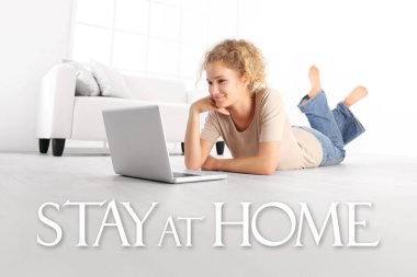 Genç bir kadın dizüstü bilgisayarla yerde oturuyor, beyaz zemin ve pencere zemininde izole edilmiş ev mesajı ile Coronavirus covid-19 önleme için sosyal medya kampanyasında kalıyor.