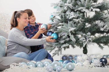 Mutlu noel aileleri, gülümseyen erkek ve kız kardeşler ağacı süslüyor mavi toplar sallanıyor ve livong odasında yerde oturuyor.