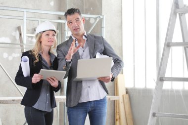 İnşaat alanında bilgisayar kullanan kadın ve erkek mimarlar veya mühendisler birlikte çalışıyorlar.