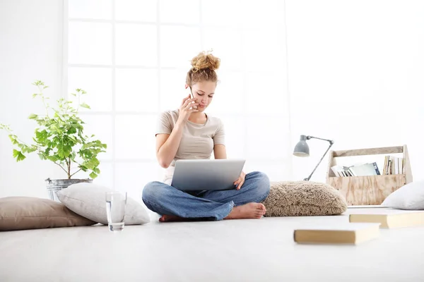 거실에 앉아서 컴퓨터로 휴대폰 통화를 여성은 컨셉에 머물러 있습니다 — 스톡 사진