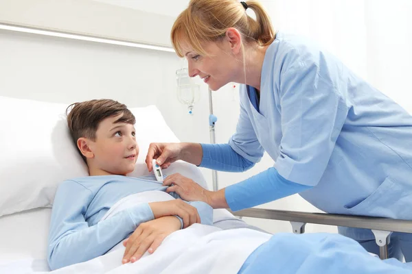快乐的孩子躺在病房的床上 护士给他量体温 — 图库照片