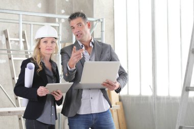 İnşaat alanında bilgisayar kullanan kadın ve erkek mimarlar veya mühendisler birlikte çalışıyorlar.