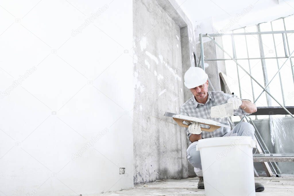 plasterer man at work, take the mortar from the bucket to plastering the wall of interior construction site wear helmet and protective gloves, and scaffolding on background