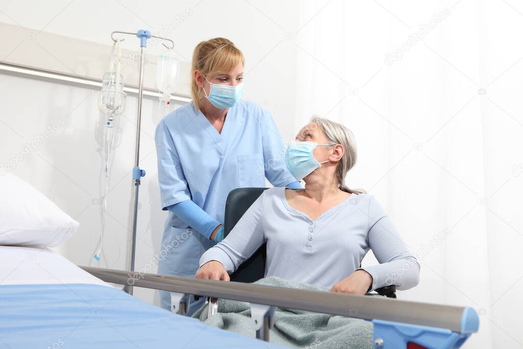 nurse take comfort elderly woman in wheelchair wearing surgical protective medical masks in hospital room, concept of isolation from corona virus covid 19