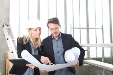 Erkek ve kadın mimarlar ya da mühendisler birlikte çalışarak inşaat alanının planlarını tartışırlar.