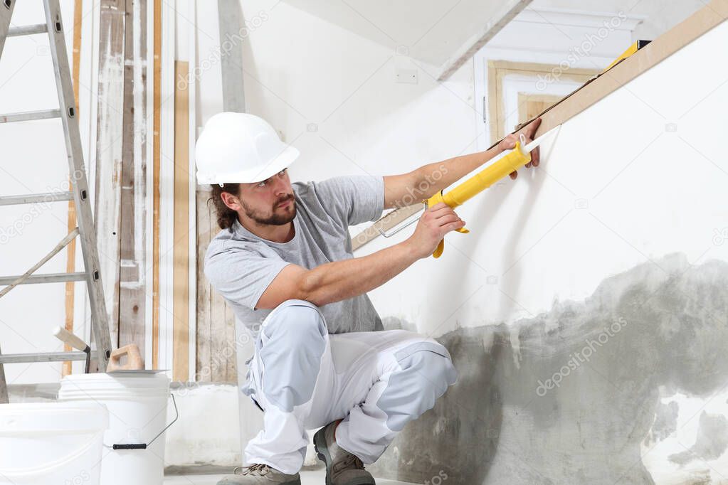 construction worker plasterer man uses caulking gun in building site of home renovation with tools and building materials on the floor