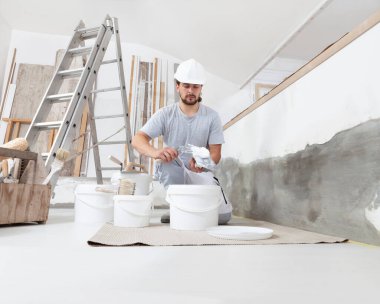 İşyerindeki alçı işçisi, kovadan alçı alıyor ve duvarı alçılamak için malanın üzerine yapıştırıyor, bir evin inşaat alanında kask takıyor.