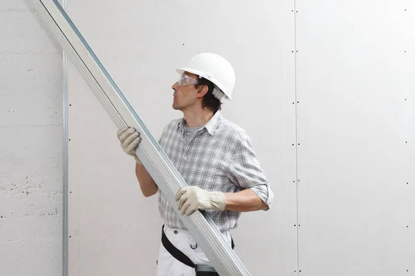安装石膏板板到墙面的干墙金属型材工人 戴着白色硬礼帽 工作手套和安全眼镜 在白色背景上与复制物分离C — 图库照片