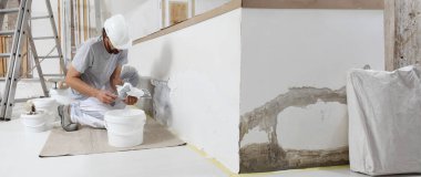 plasterer man at work, take the mortar from the bucket with trowel to plastering the wall of interior construction house site and wear helmet, panoramic image clipart