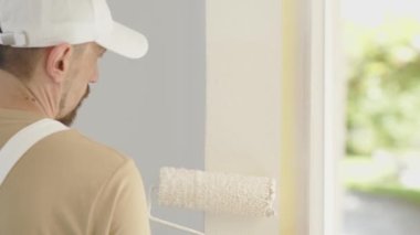 Boyacı adam dekoratörlüğü, yenileme işi, duvarda paten boyası, arka planda yeşile boyanmış pencere, kapat.