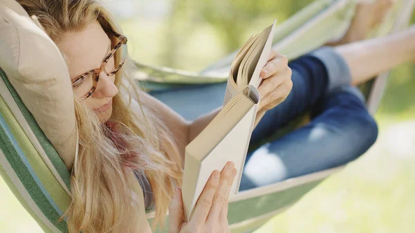 Smiling Blonde Woman Eyeglasses Reading Book Relaxing Hammock Garden Leisure — Stock Photo, Image