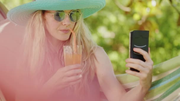 Mujer Rubia Sonriente Con Gafas Sol Usando Teléfono Inteligente Relajándose — Vídeos de Stock