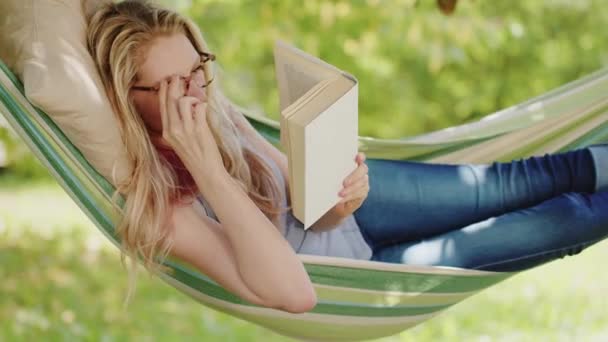 Smiling Blonde Woman Eyeglasses Reading Book Relaxing Hammock Garden Leisure — Stock Video