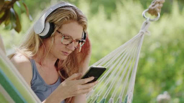 Χαμογελαστή Ξανθιά Γυναίκα Που Φοράει Γυαλιά Χρησιμοποιώντας Smartphone Ακούγοντας Μουσική — Αρχείο Βίντεο