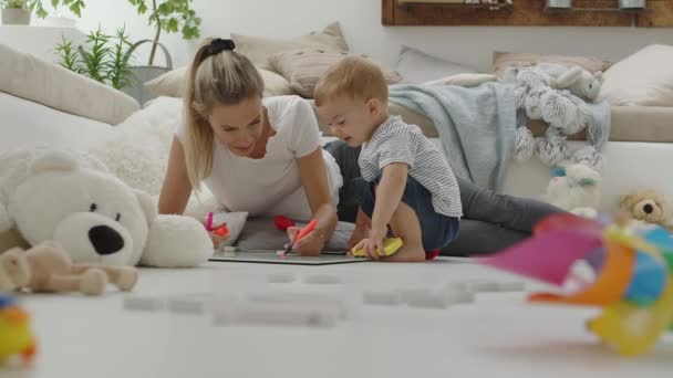 快乐的妈妈和她的孩子一起玩 带着彩笔和白板 带着教育意义的学习游戏 坐在家里枕头和动物的毛绒绒中间 健康而又关心成长的概念 — 图库视频影像
