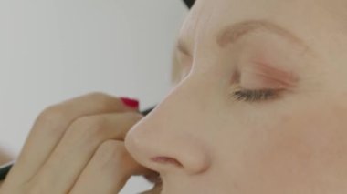 Makyajcının elleri fırçayla göz farı sürer, beyaz bir sarışının yüzünü mavi gözlerle kapatır.