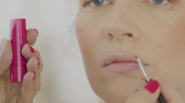 Makyajcının elleri ruj sürerken dudakları fırçalanmış, yüzü beyaz, mavi gözlü sarışın bir kadın, kapat. 