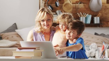 Evde mutlu bir aile, oğlu ve kızı olan bir anne bilgisayar kullanarak eğleniyor, çocuklu bir ebeveyn internette internette geziniyor, çocuk öğrenci monitörü işaret eden bir şey gösteriyor.