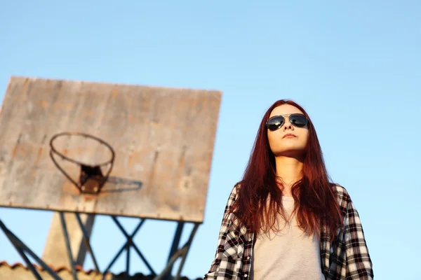 Girl with sunglasses looking at the sky behind with old basketba — Stock Photo, Image
