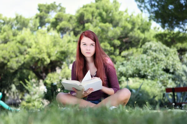 Student sedí v parku s knihou vyhledávání — Stock fotografie