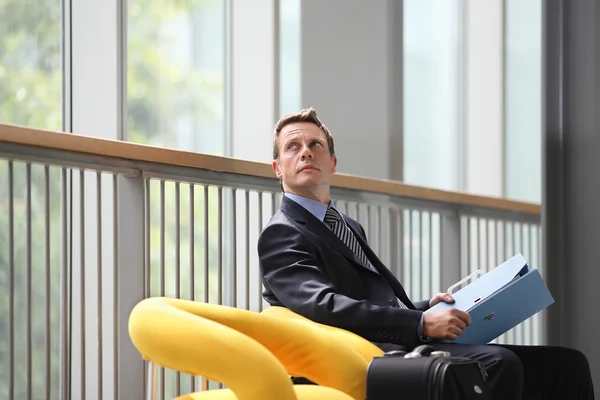 Geschäftsmann mit blauem Ordner in der Hand im Wartezimmer sitzend — Stockfoto