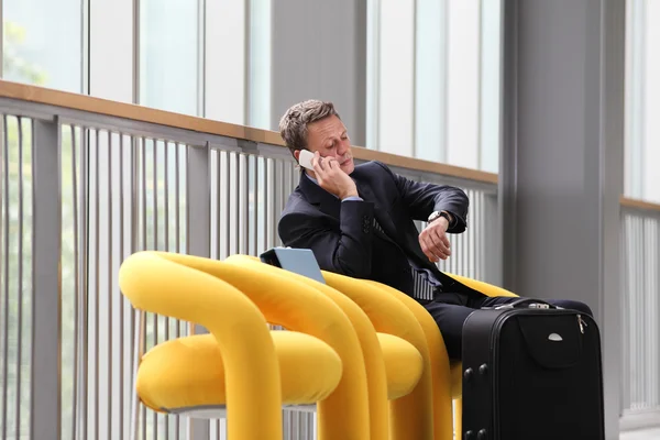 Empresario sentado hablando por teléfono y mirando el reloj, en un viaje de negocios — Foto de Stock