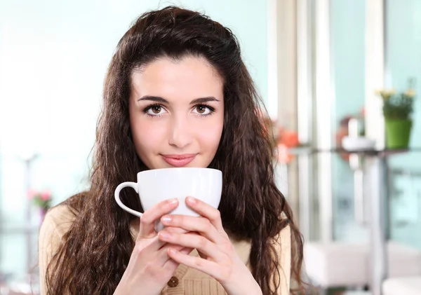 Девушка улыбается в кофе напиток с чашкой в руке — стоковое фото