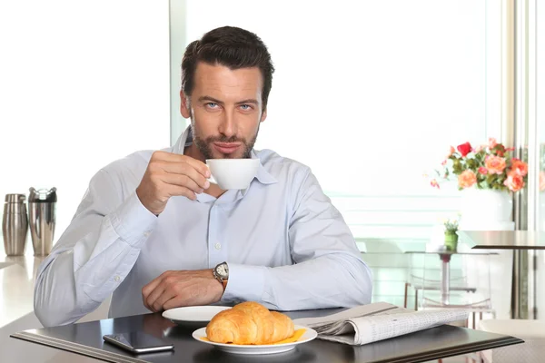 Hombre tomando café en la cafetería con croissant y periódico —  Fotos de Stock