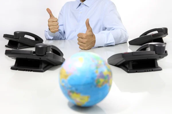 Globe och gillar hand med office telefoner på skrivbord, global support — Stockfoto