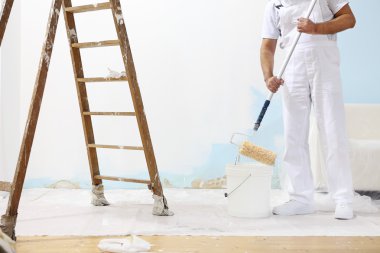Ressam adam iş yerinde rengi boya silindiri ile kova alır.