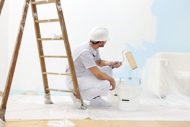 Ressam adam iş yerinde rengi boya silindiri ile kova alır.