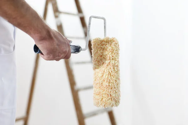 Pintor homem no trabalho com um rolo de pintura e escada, close-up — Fotografia de Stock