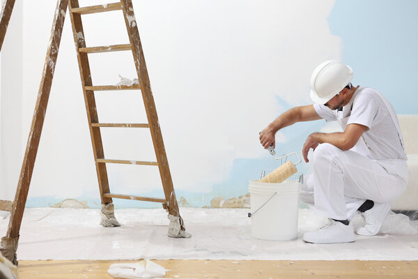 Painter man at work takes the color with paint roller from bucket