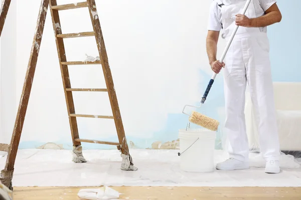 Ressam adam iş yerinde rengi boya silindiri ile kova alır. — Stok fotoğraf