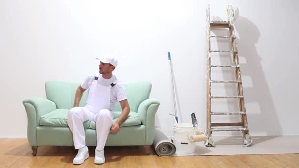 Maler bei der Arbeit, fertig mit der Arbeit und legt sich auf die Couch — Stockvideo
