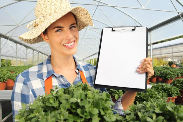 Sonriente mujer trabajando en invernadero, muestra el portapapeles en blanco — Foto de Stock
