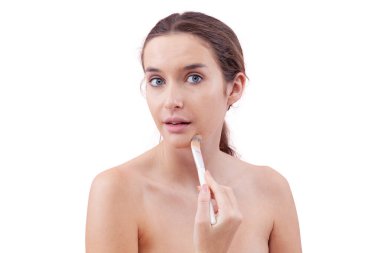 Yüzünde makyaj fırçası olan doğal cilt bakımlı genç bir kadın. Pürüzsüz, kusursuz bir ten. Temiz güzellik rutin konsepti, beyaz arka planda izole edilmiş, kameraya bakıyor