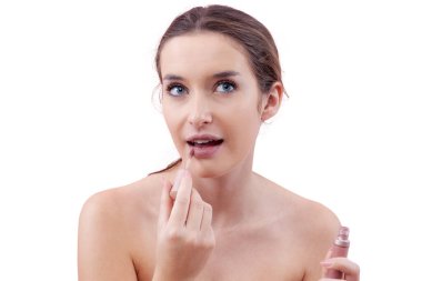 Dudak fırçası aplikatörüyle dudaklarına ruj süren genç bir kadın makyaj rutininin bir parçası olarak. Taze, doğal görünümlü bir güzellik konsepti. Beyaz arka planda izole edilmiş, temiz ve minimal