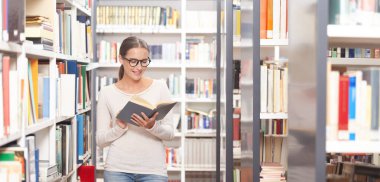 Modern bir kütüphanede kitap okuyan gözlüklü genç bir kadın. Arkaplanda renkli kitaplarla dolu kitaplıklar. Öğrenim, eğitim, öğrenim, bilgi ve akademik yaşam tarzı kavramı