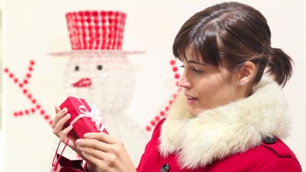 Mujer de Navidad abre bolsa con regalo y sonrisas, con muñeco de nieve en el fondo — Vídeo de stock