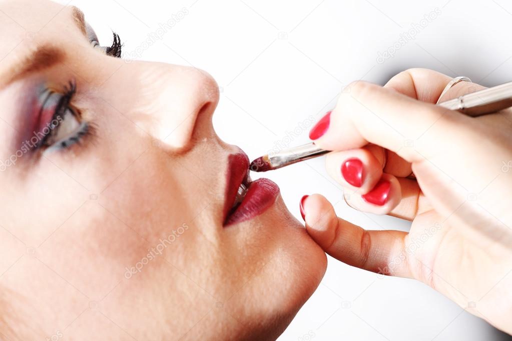 makeup artist applying lipstick on model lips with brush, closeu